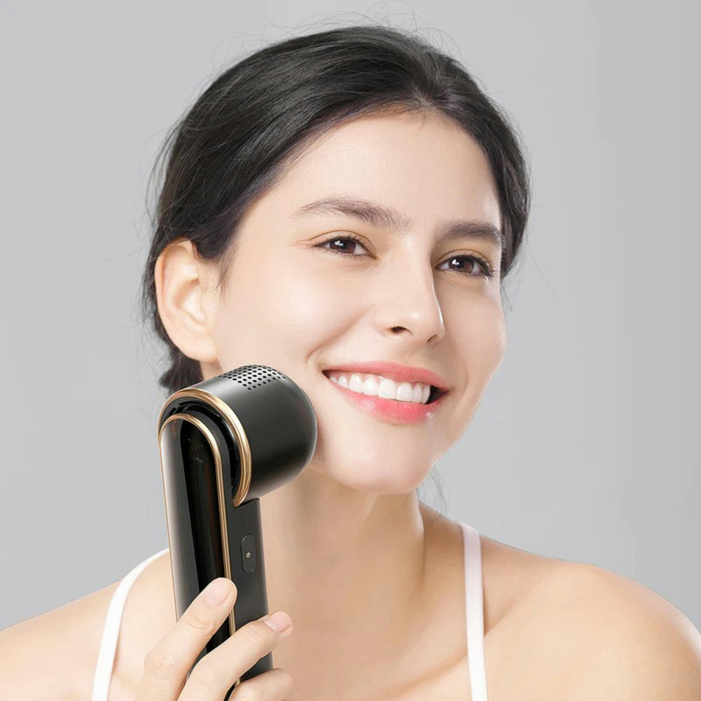 A woman is smiling while holding a device to her face.