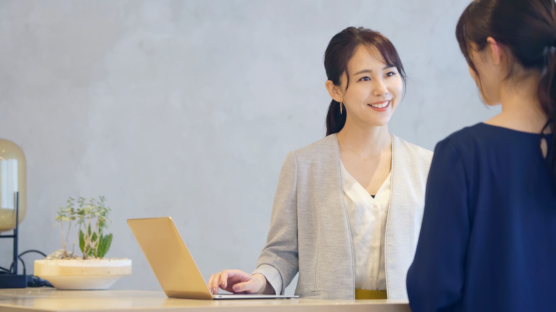 A woman is sitting at a counter with a laptop and talking to another woman.