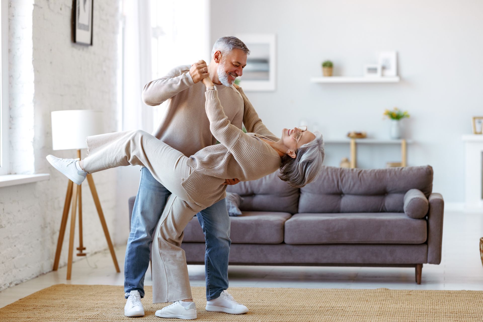 An elderly couple is dancing together in a living room.