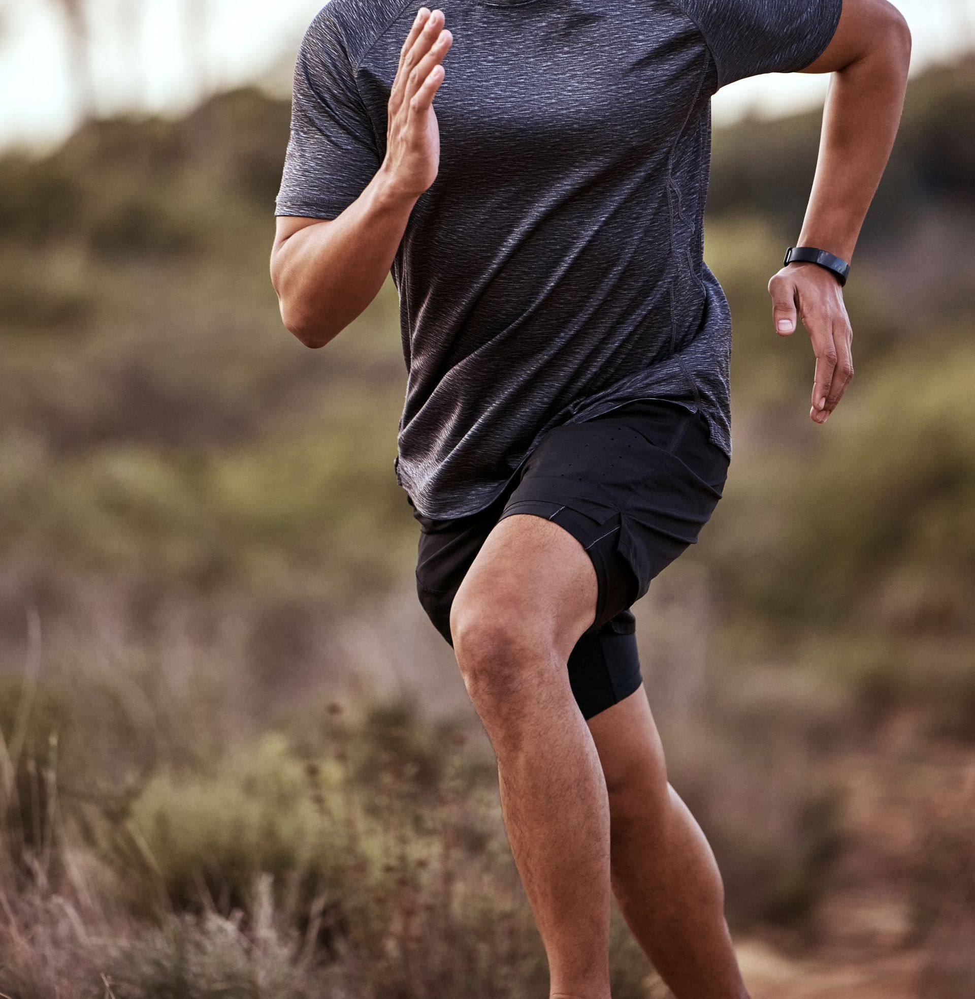 A man in a gray shirt and black shorts is running on a dirt road.