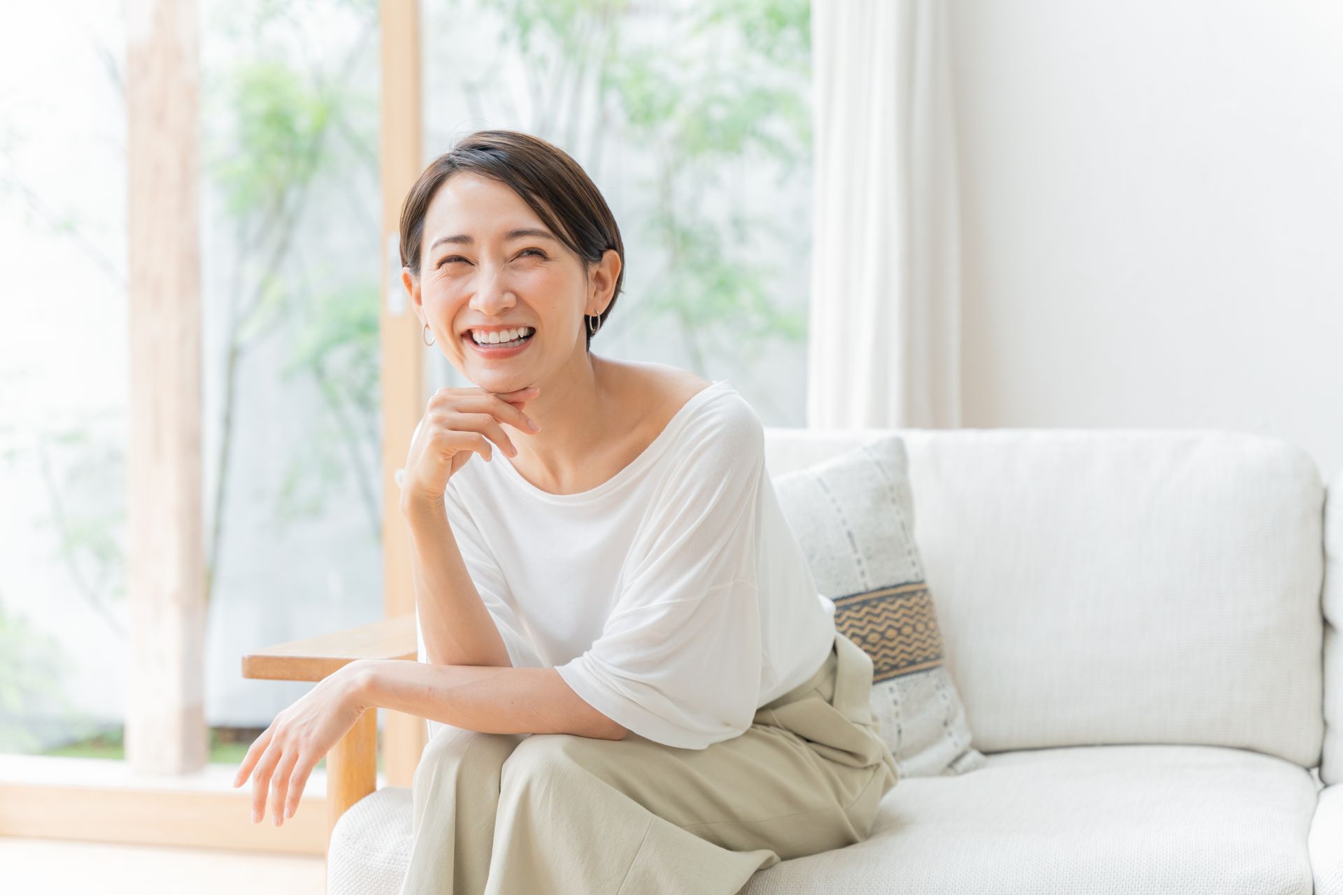 A woman is sitting on a couch in a living room smiling.
