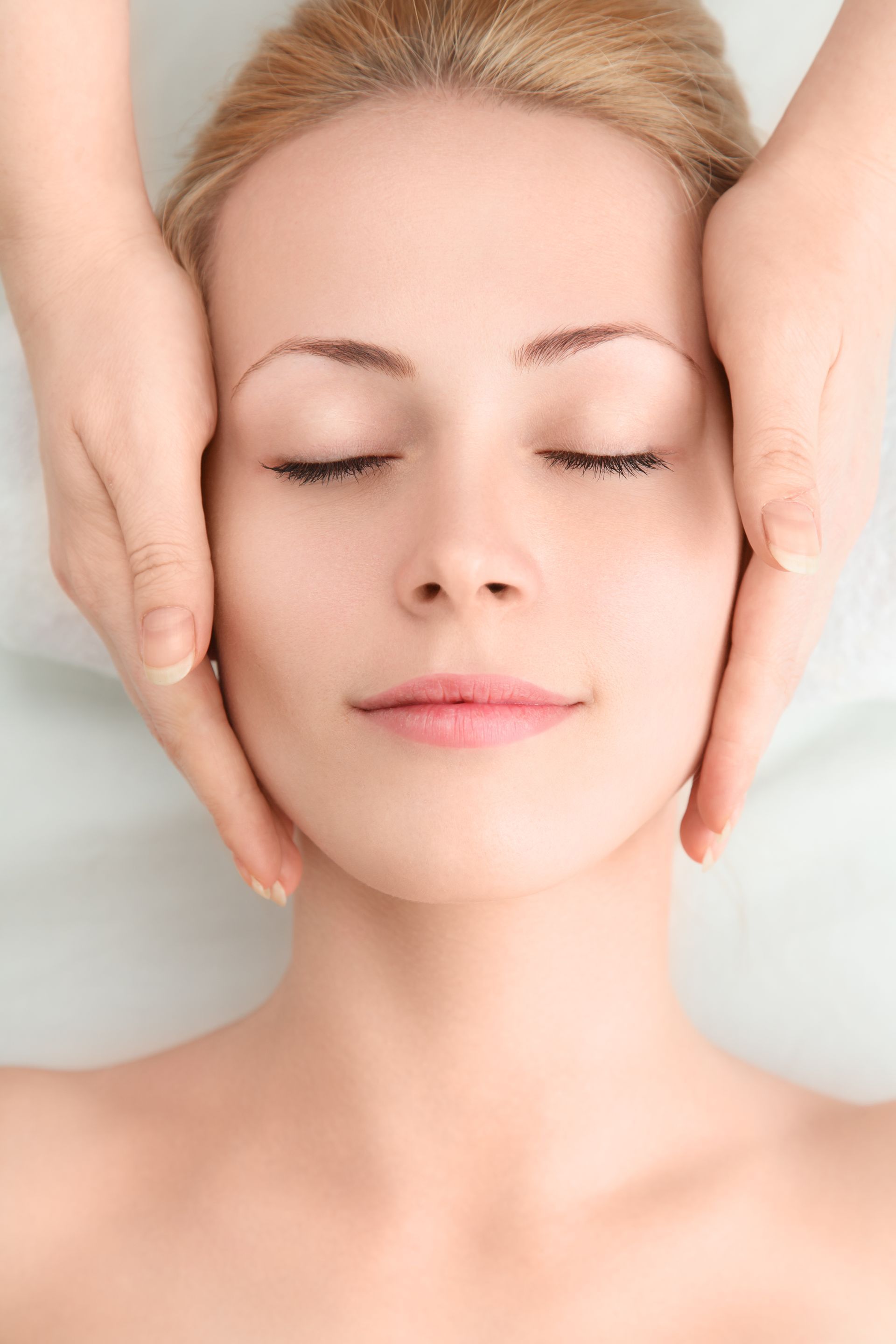 A woman is getting a facial massage at a spa with her eyes closed.