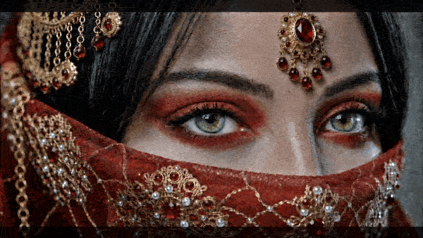 Portrait of a jeweled woman with glittery makeup, centered against a dark, bokeh-lit background