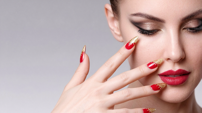 Close-up of a woman with red nails and lipstick touching her face on a soft gray background