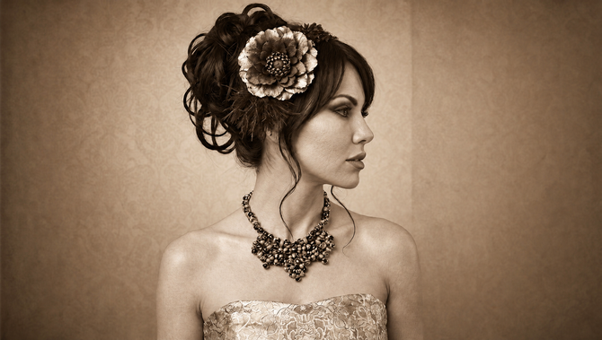 Sepia-toned portrait of a woman in profile with an ornate floral hair accessory and necklace, against a textured backdrop