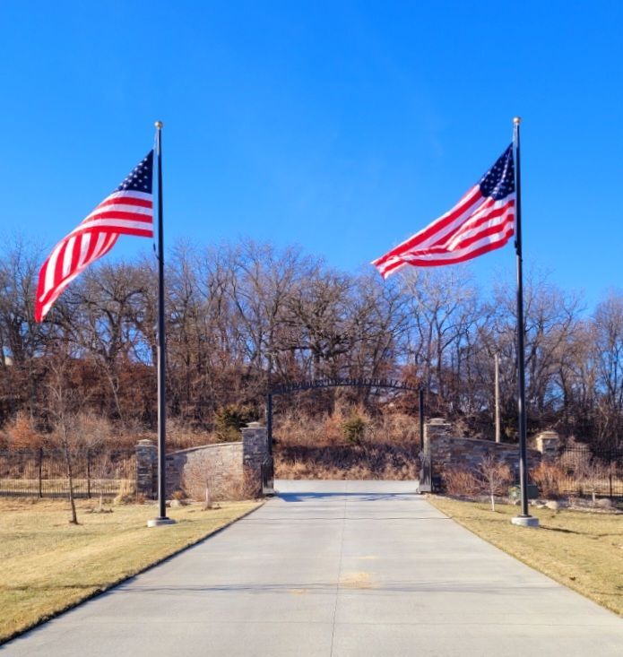 Two U.S. flags on poles lining a driveway under a clear blue sky