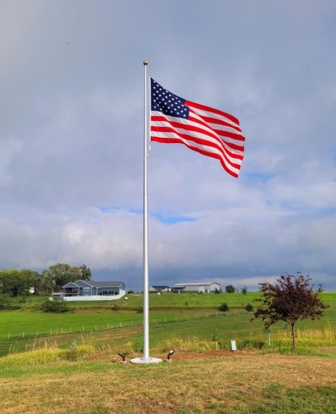 American flag waving on a pole in a grassy field under a cloudy sky