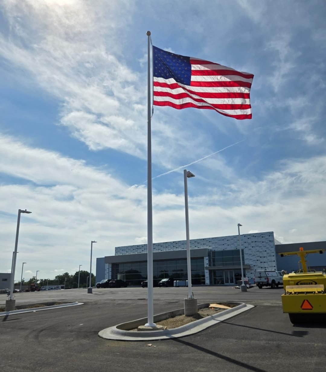 Large American flag on a pole outside a modern industrial building under a cloudy sky