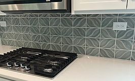 Kitchen backsplash with gray and white patterned tiles, white cabinets, and gas stovetop.