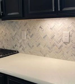 Kitchen backsplash with herringbone tile, white countertops, and black cabinets.