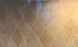 Tan and cream-colored arabesque tile backsplash with light grout.