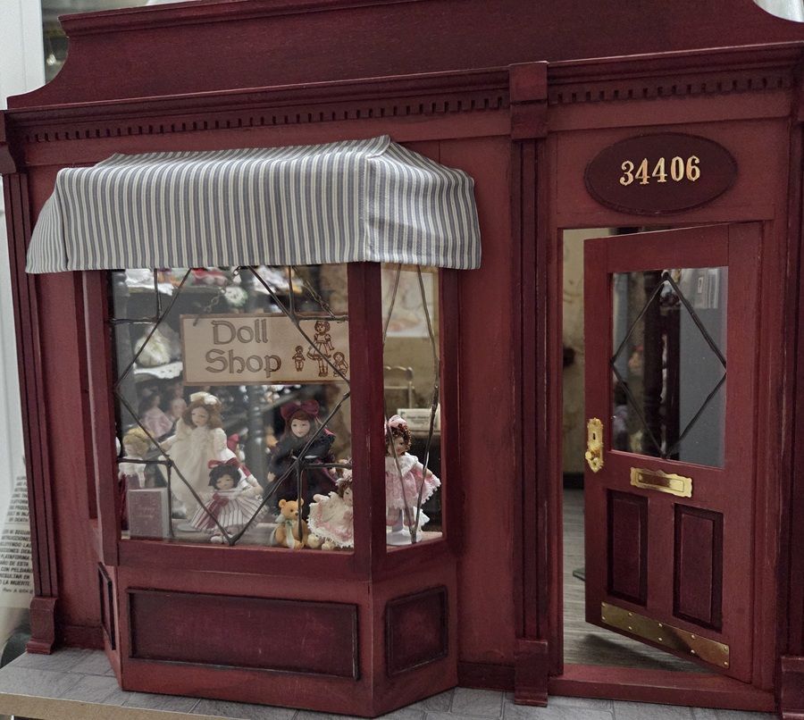 Red storefront with striped awning and display window for a doll shop, door numbered 34406