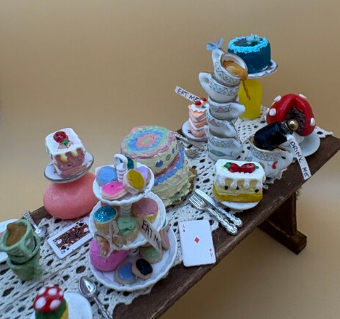 Miniature desserts and pastries displayed on a bench, including colorful cakes, teacups, and a playing card.