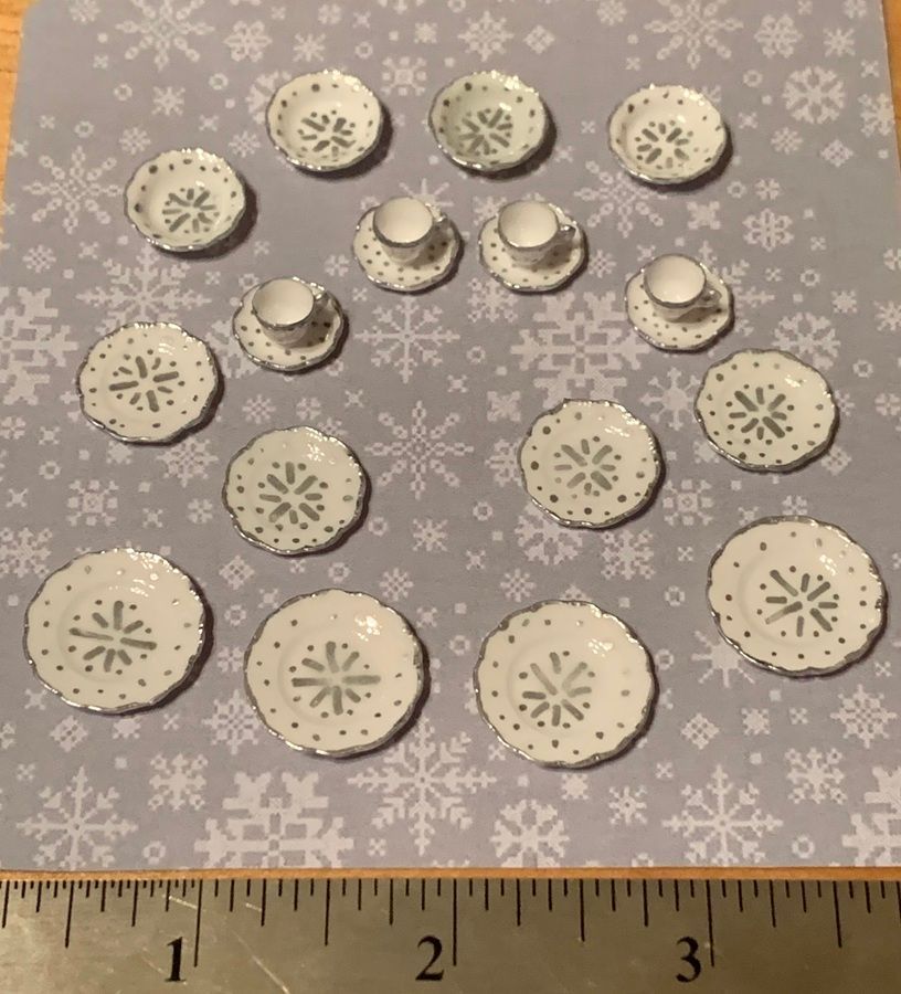 Assorted small white snowflake-shaped ornaments arranged on a gray snowflake-patterned surface with a ruler below
