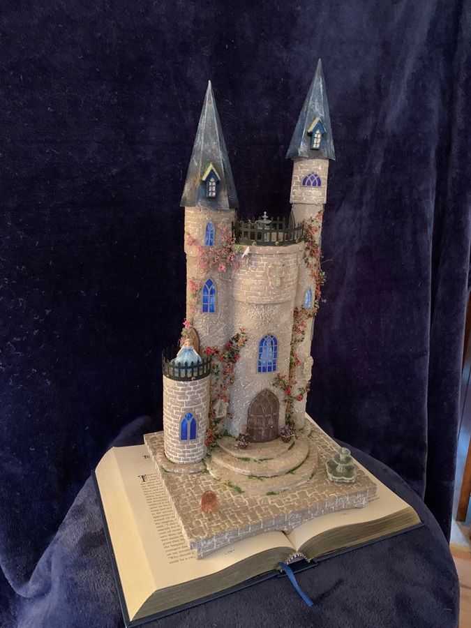 Miniature castle model with tall towers, perched on an open book against a dark background