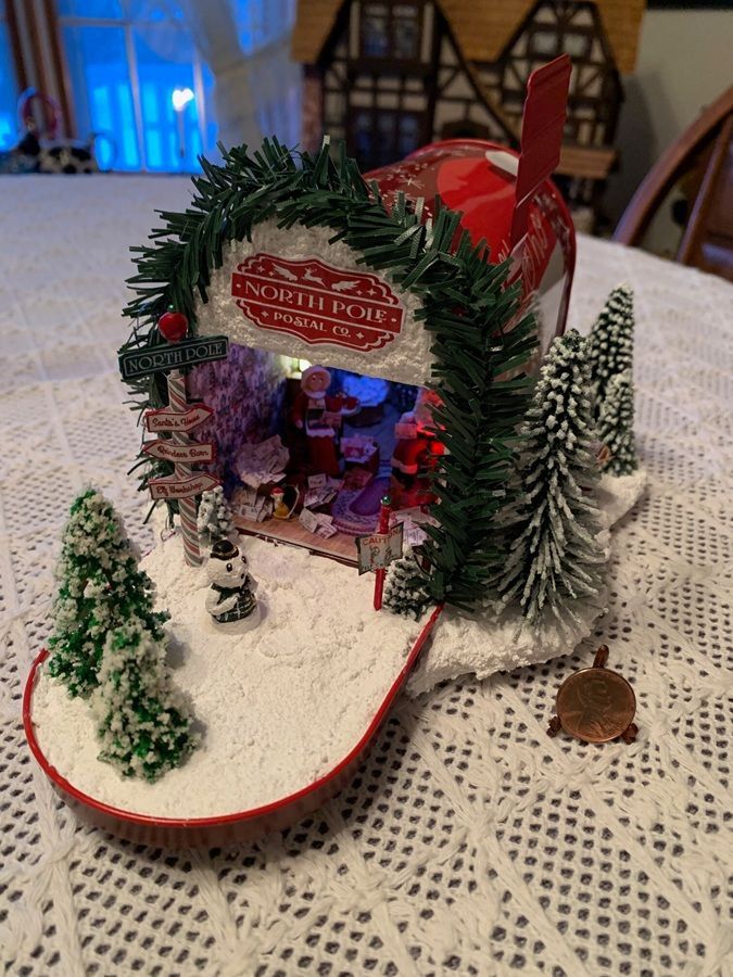 Miniature Christmas village display with a lit red-and-green cabin, trees, and snowy ground