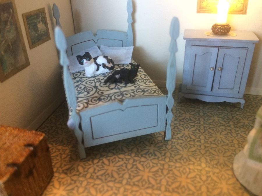 Two cats resting on a white bed in a cozy bedroom with patterned carpet and a small nightstand