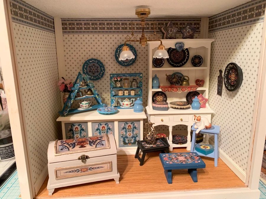 Miniature diorama in a wooden frame with a small ship finial, showing a figurine and stacked boxes inside.