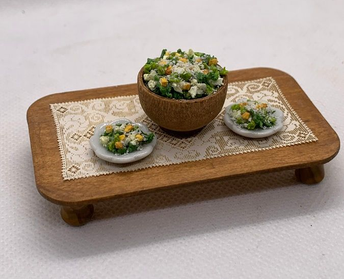 Mini wooden tray with lace doily and three bowls of green salad on a white background