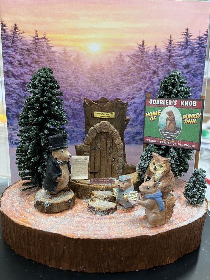 Miniature woodland scene with squirrels by a tiny door, tree, and sign against a snowy sunset backdrop
