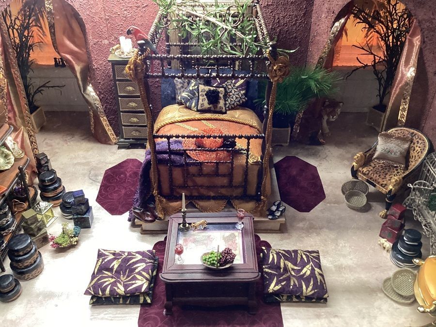 Decorative miniature room with a bed, bench, tables, lanterns, and potted plants in warm earthy tones