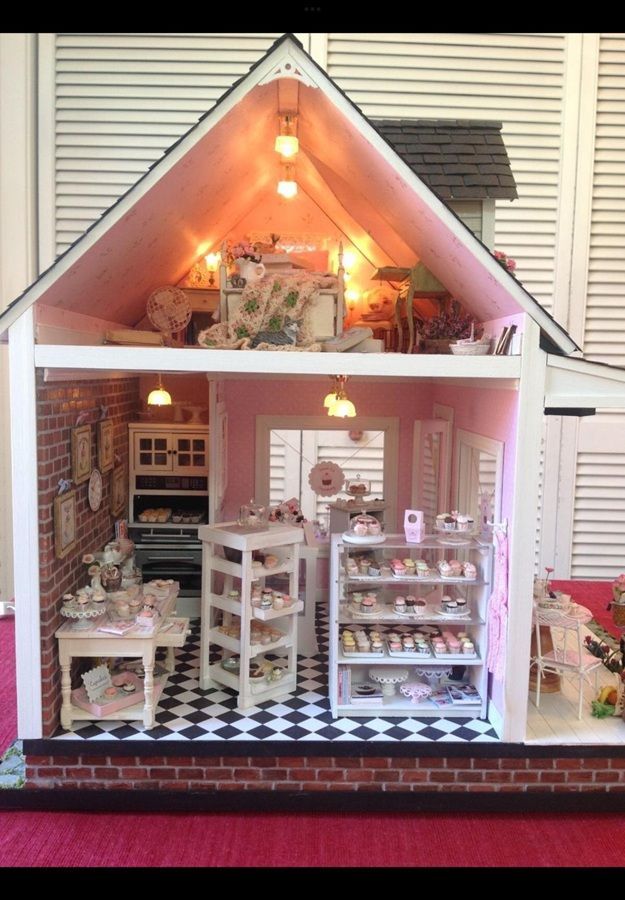 Miniature pink dollhouse bakery with shelves of cakes, warm lights, and black-and-white floor tiles
