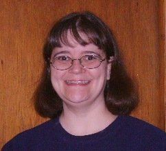 Smiling person with glasses and dark hair in front of a wooden background