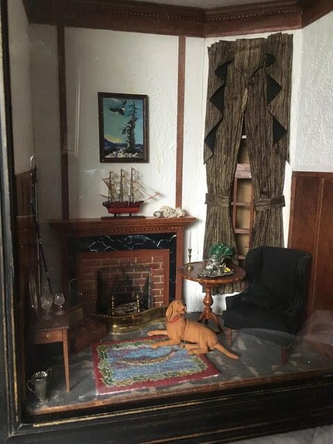 Miniature vintage-style living room with two seated dolls, black-and-red furniture, and ornate wall decor