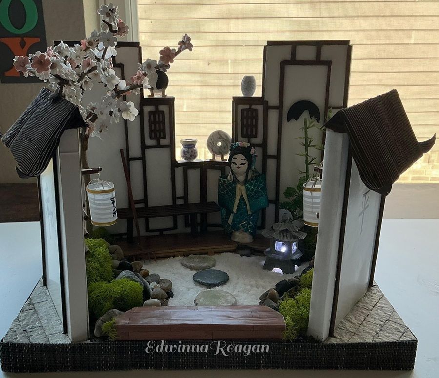 Miniature Japanese garden display with lanterns, cherry blossoms, stepping stones, and a geisha figure