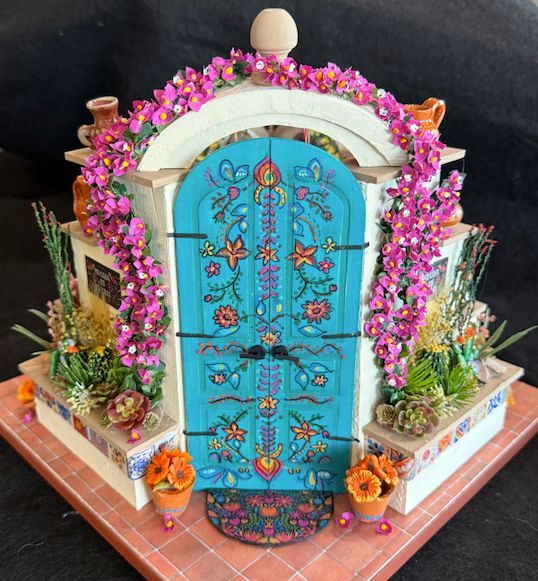 Decorated blue miniature door surrounded by pink garland and flowers on a small display base