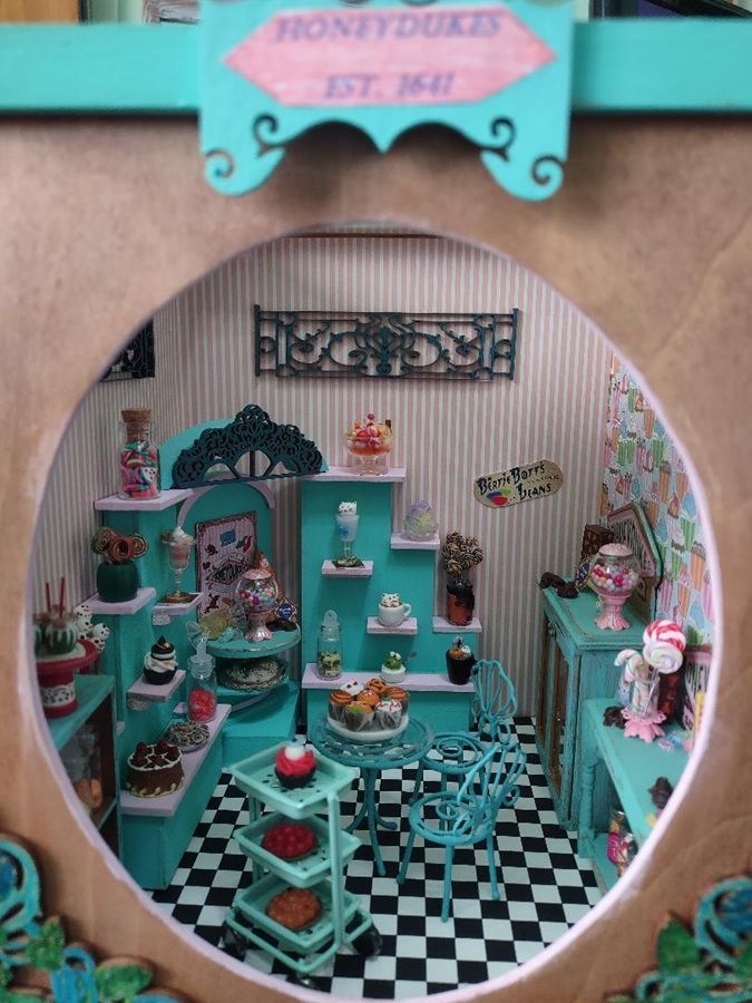 Miniature turquoise dollhouse bakery with checkered floor and tiny cakes on shelves and tables