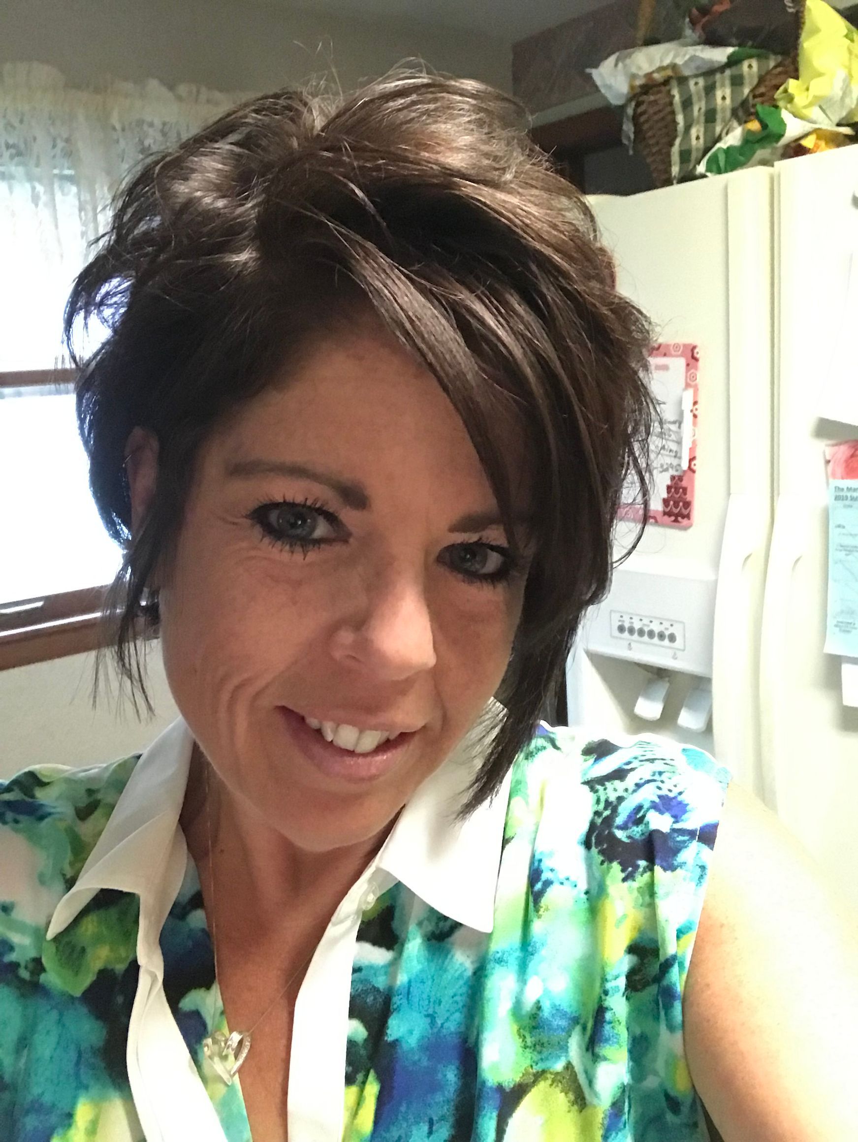 Smiling woman with dark hair in a colorful blouse standing in a kitchen