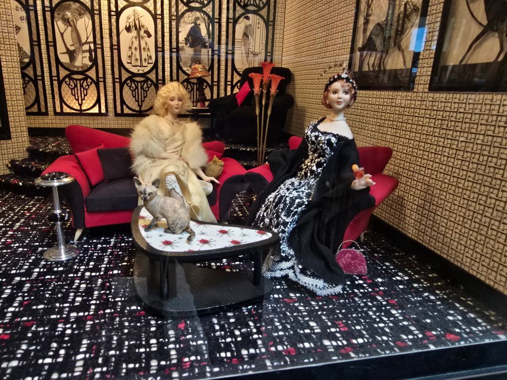 Two ornate mannequins seated on a red couch beside a small round table in a patterned lounge
