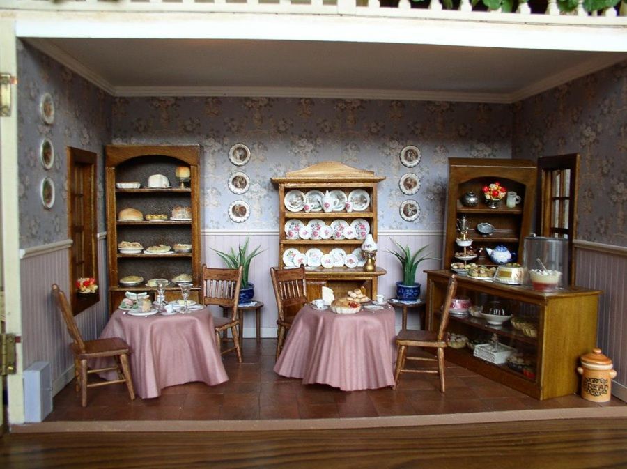 Miniature dining room display with shelves of dishes, pink tablecloths, and a wooden cabinet on the right.