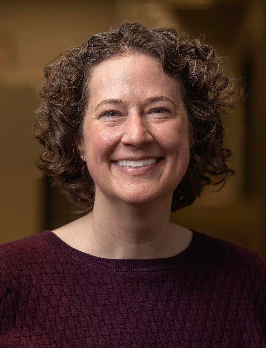 Smiling person with curly hair in a burgundy sweater against a warm indoor background
