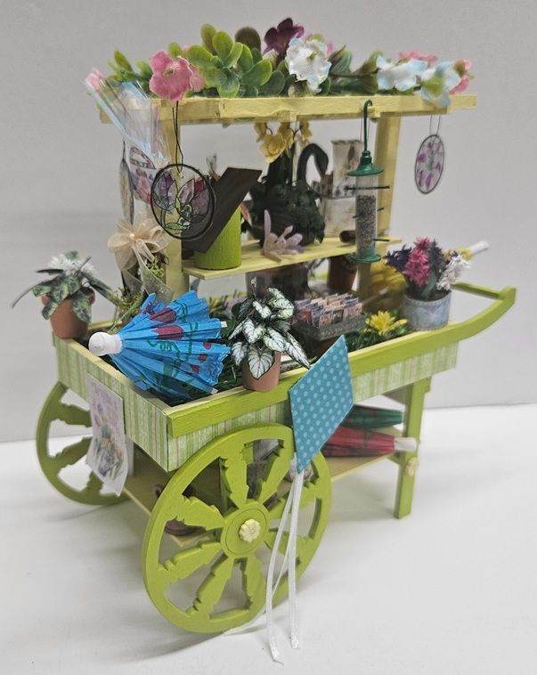 Green decorative cart filled with flowers and trinkets, with large lime wheels and a striped canopy