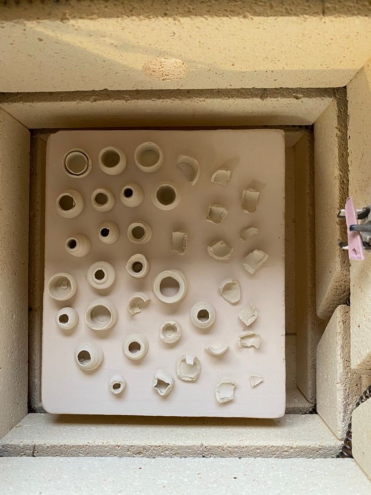 White ceramic tile with many small round holes inside a square kiln or frame.