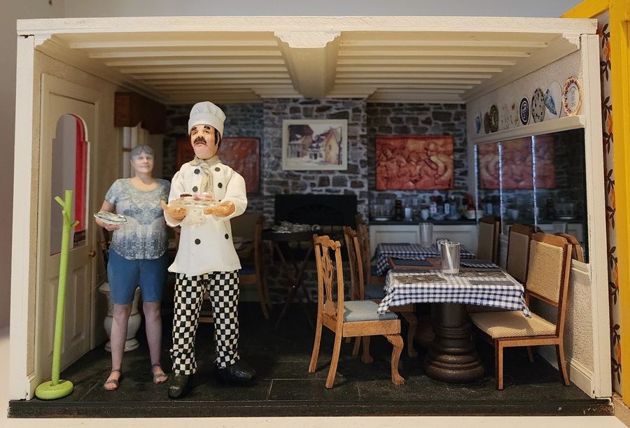 Miniature cafe diorama with two figures behind a small table and chairs in a cozy indoor setting