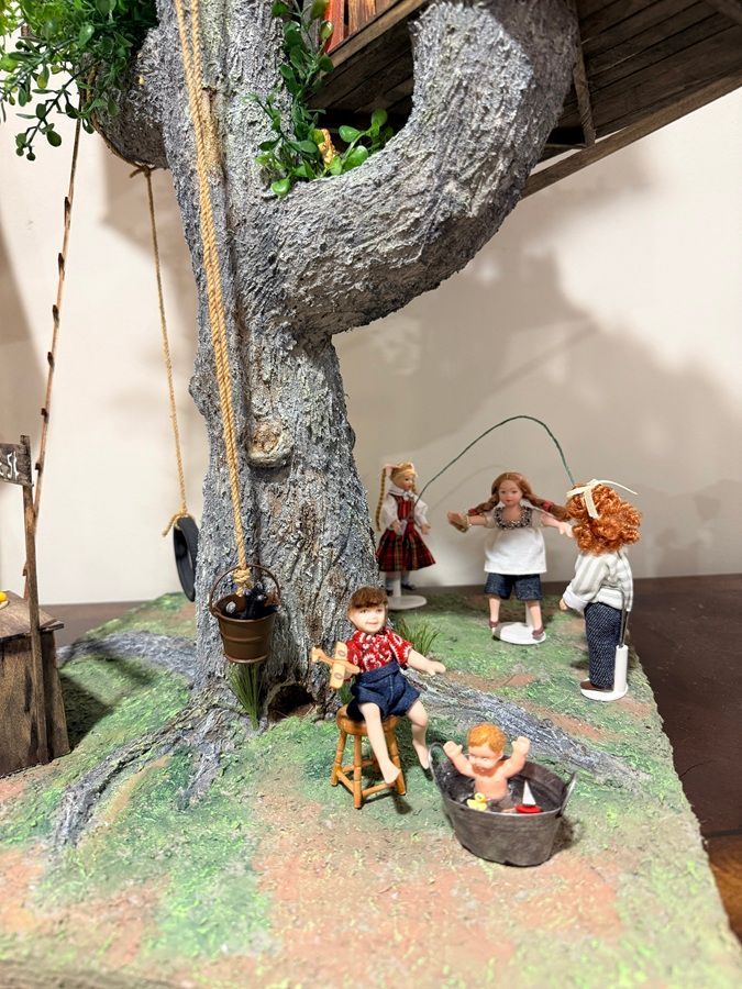 Miniature woodland scene with figurines around a large tree trunk and a small basket on the ground