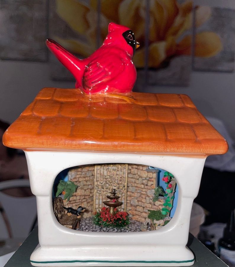 Red bird figurine on an orange-tiled ceramic house with a tiny garden scene window.