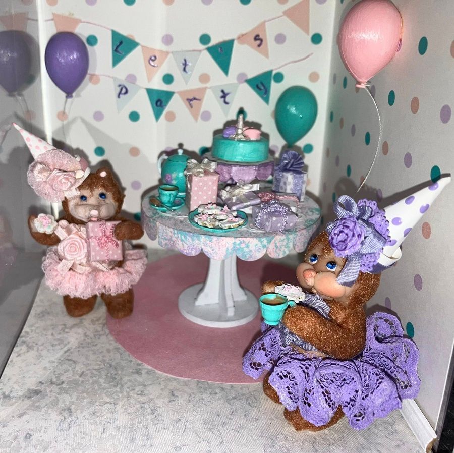 Two teddy bears at a pastel tea party table with balloons and party decor