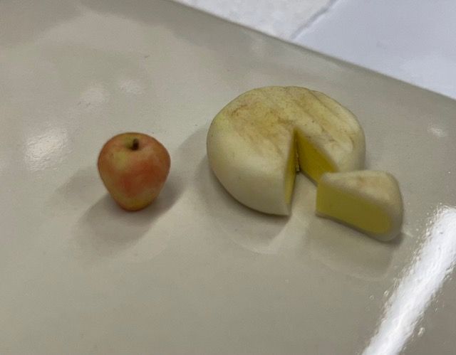 A small apple beside a sliced white fruit with one wedge removed on a white table.