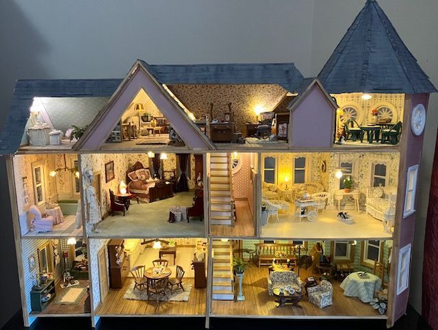 Dollhouse cross-section showing lit rooms, stairs, and miniature furniture in a two-story house interior