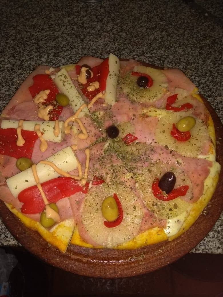 Pastel redondo decorado con fruta, trozos de chocolate y glaseado de colores sobre un plato.