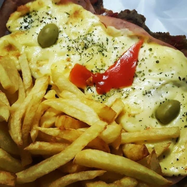 Papas fritas cubiertas con queso derretido, aceitunas verdes y salsa roja en un plato.