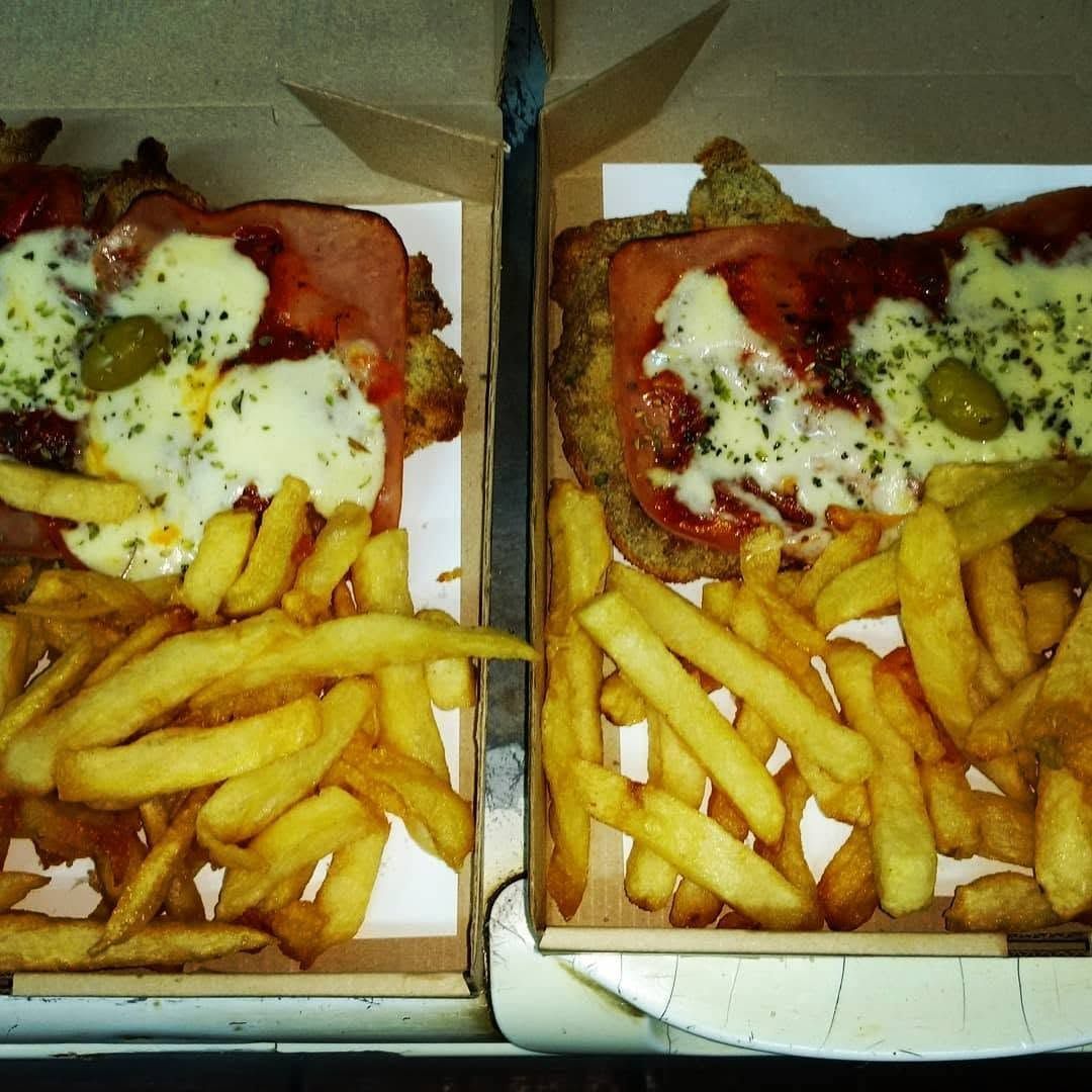Dos porciones de pizza para llevar con papas fritas en cajas abiertas, cubiertas con queso derretido y salsa.