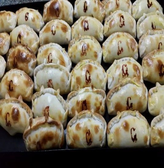Bandeja de bollos o empanadillas redondas, doradas y glaseadas, horneadas en filas y dispuestas con esmero.