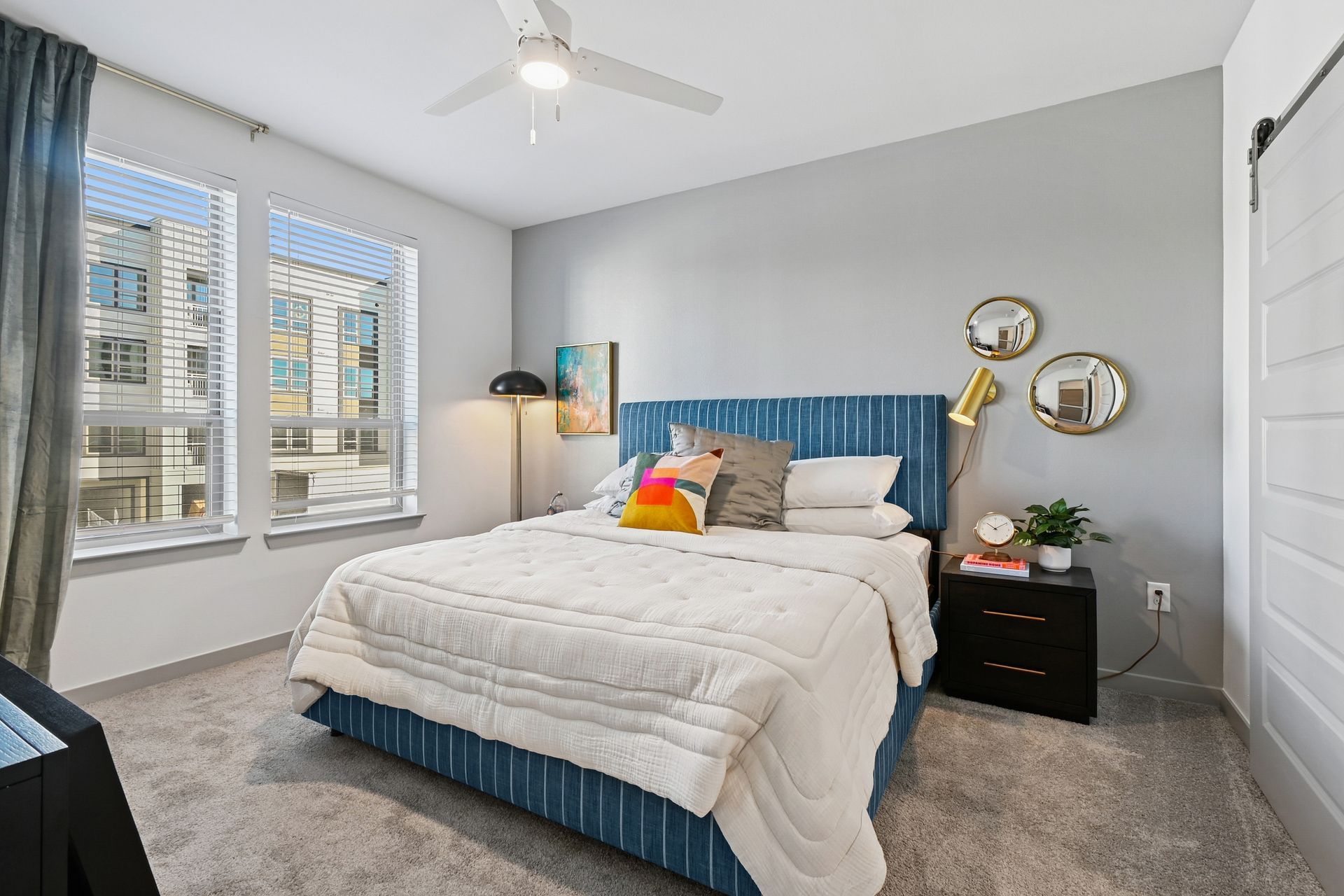 Bedroom with blue bed, gray walls, two windows, and black nightstand  at  One90 Firewheel Garland, TX.