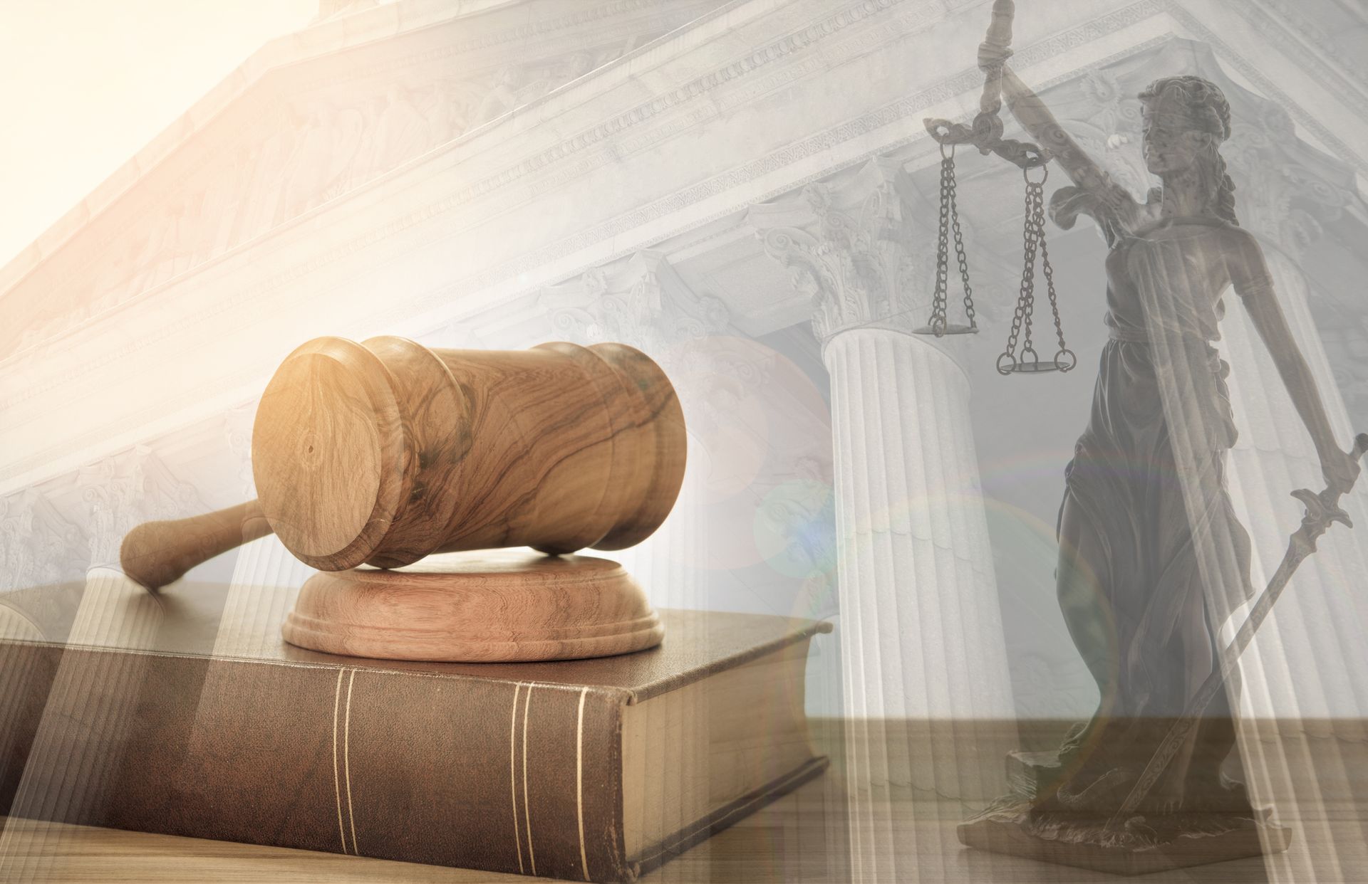 A wooden gavel is sitting on top of a book with a statue of justice in the background.
