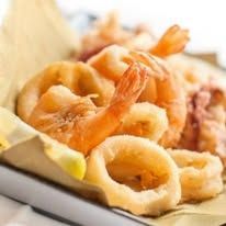 Anelli di gamberi e calamari fritti serviti su un piatto con spicchi di limone.